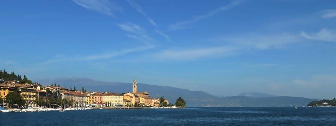 Last Minute beliebte Urlaubsziele am Gardasee -  Mit einer Fläche von 370 km² ist der Gardasee der größte See Italiens. Es liegt am Fuße der Alpen und erstreckt sich über drei Staaten: Lombardei, Venetien und Trentino. Die maximale Tiefe des Sees beträgt 346 m, er hat eine längliche Form und sein nördliches Ende ist sehr schmal. Dort ist der See von den Bergen der Gruppo di Baldo umgeben. Du trittst aus deinem gemütlichen Hotelzimmer und es begrüßt dich die warme italienische Sonne. Du blickst auf den atemberaubenden Gardasee, der in zahlreichen Blautönen schimmert - von tiefem Dunkelblau bis zu funkelndem Türkis. Majestätische Berge umgeben dich, während die Brise sanft deine Haut streichelt und der Duft von blühenden Zitronenbäumen deine Nase kitzelt. Du schlenderst die malerischen, engen Gassen entlang, vorbei an farbenfrohen, blumengeschmückten Häusern. Vereinzelt unterbricht das fröhliche Lachen der Einheimischen die friedvolle Stille. Du fühlst dich wie in einem Traum, der nicht enden will. Jeder Schritt führt dich zu neuen Entdeckungen und Abenteuern. Du probierst die köstliche italienische Küche mit ihren frischen Zutaten und verführerischen Aromen. Die Sonne geht langsam unter und taucht den Himmel in ein leuchtendes Orange-rot - ein spektakulärer Anblick.
